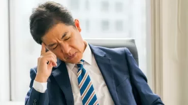 ストレスを抱えるスーツ姿のビジネスマンが椅子に座っている。