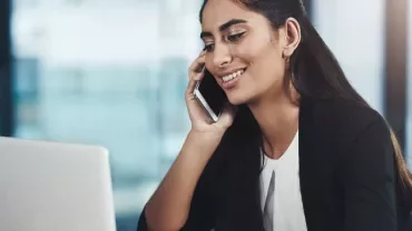 Woman smiling while talking on the phone and using a laptop.