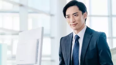 スーツを着たビジネスマンがデスクで微笑んでいる。