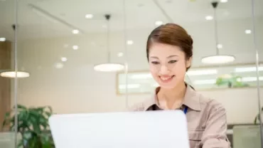 Woman smiling while using a laptop in a bright office.
